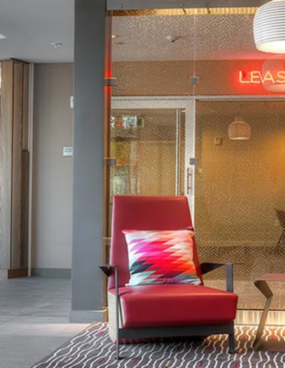 The lobby of a hotel with red chairs and a glass door.