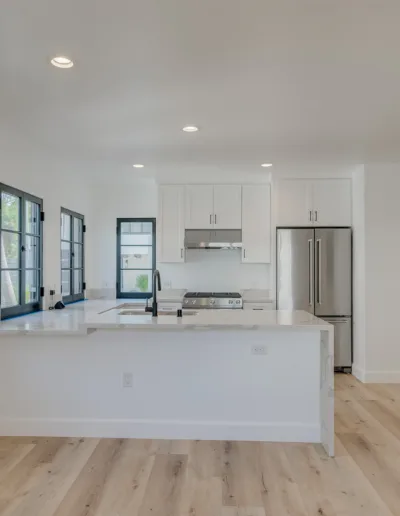 An empty kitchen with white cabinets and wood floors.