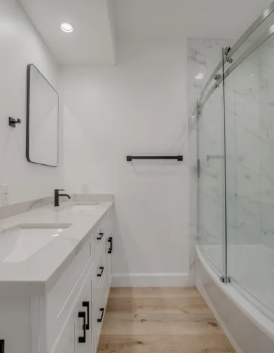 A white bathroom with two sinks and a walk in shower.