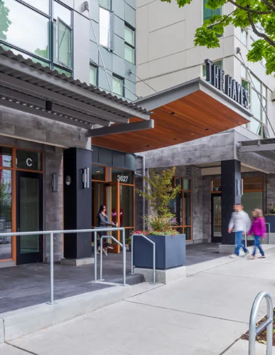 Two people walking down the sidewalk of a building.