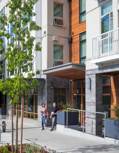 Two people walking down a sidewalk in front of an apartment building.