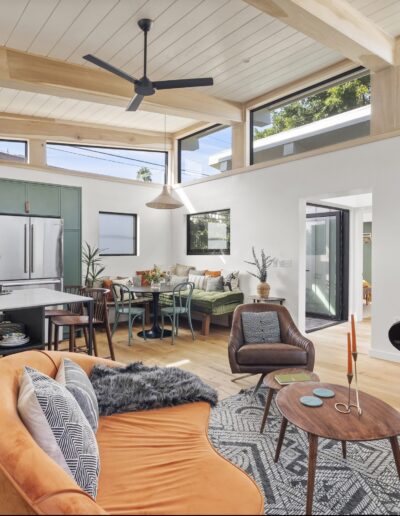 Open-concept living area featuring a kitchen with green cabinets, a dining table, a cozy seating area with an orange sofa and armchair, and a suspended fireplace. Large windows provide natural light.